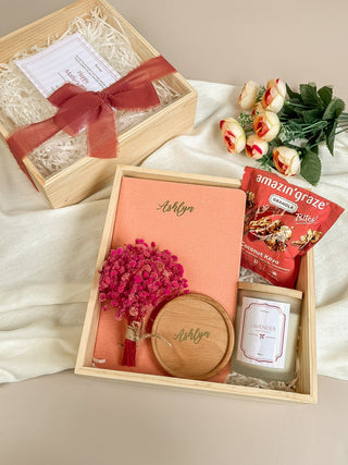 Gift box with snacks, flowers, and a card on a white surface