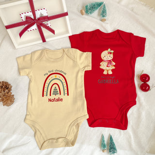 Two baby onesies with Christmas-themed designs on a white surface with decorative items.